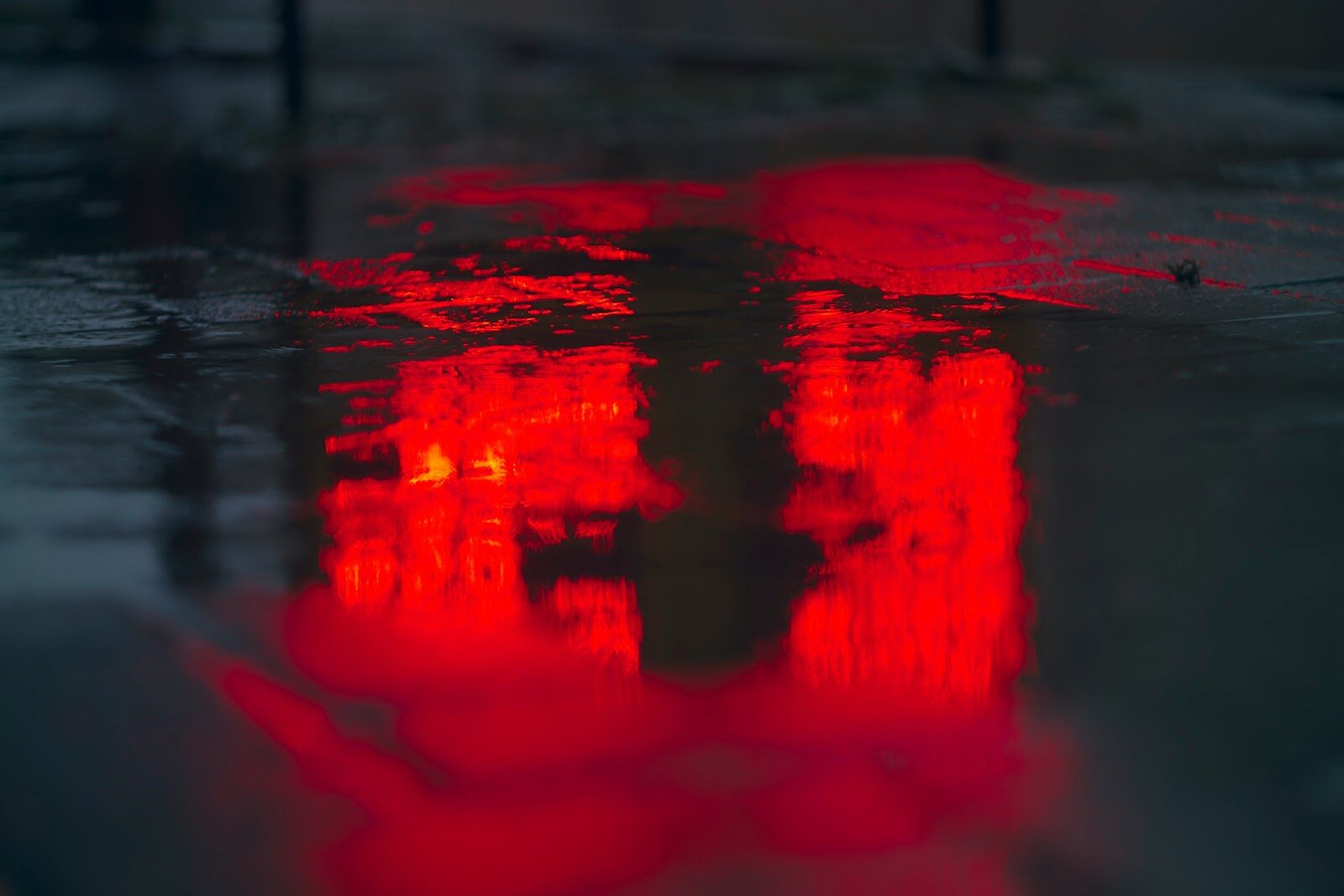 Bright red neon light reflecting on a wet dark asphalt surface